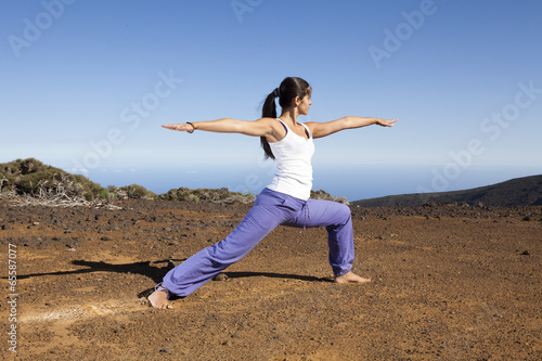 Young woman practicing yoga warrior pose on a desert mountain