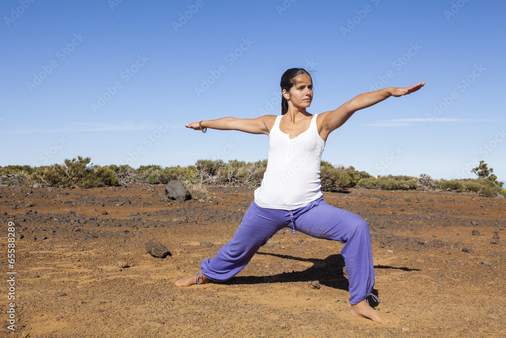 Young woman practicing yoga warrior pose on a desert mountain Young woman practicing yoga warrior pose on a desert mountain