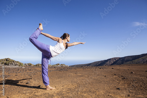 Young attractive woman doing dancers yoga pose outdoors on a des
