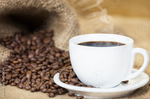 Cup of hot coffee with coffee beans, in front of canvas sack. © narstudio