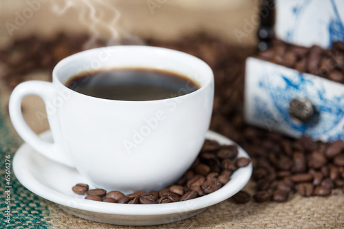 Cup of coffee surrounded with coffee beans on a wooden table.