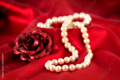 Pearl necklace and red rose on red silk.