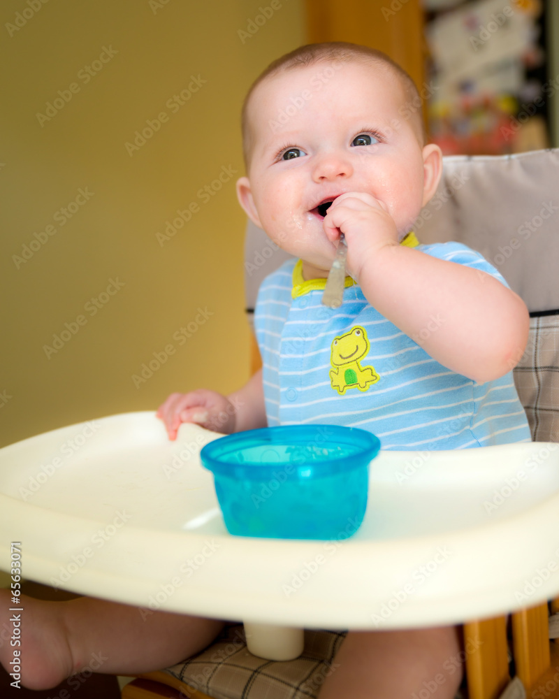 Happy baby infant boy eating meal while sitting in high chair Happy baby infant boy eating meal while sitting in high chair