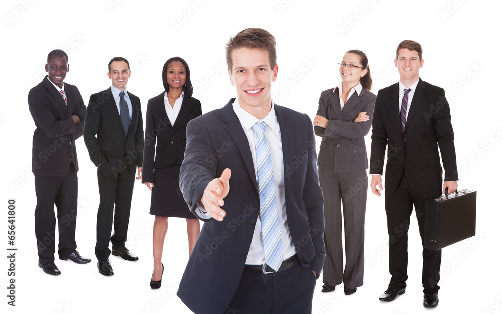 Businessman Offering Handshake With Team In Background Businessman Offering Handshake With Team In Background