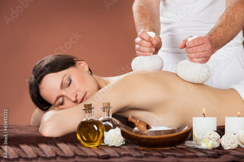 Woman Receiving Massage With Herbal Compress Stamps At Spa