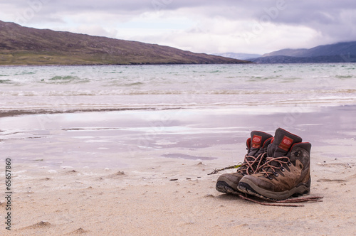 Pair of trekking boots on a remote beach with sea and mountains