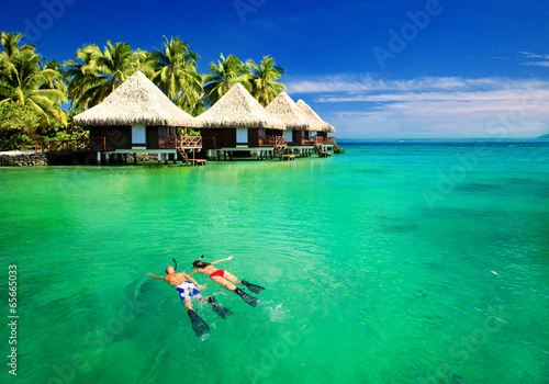 Couple snorkling in lagoon with over water bungalows