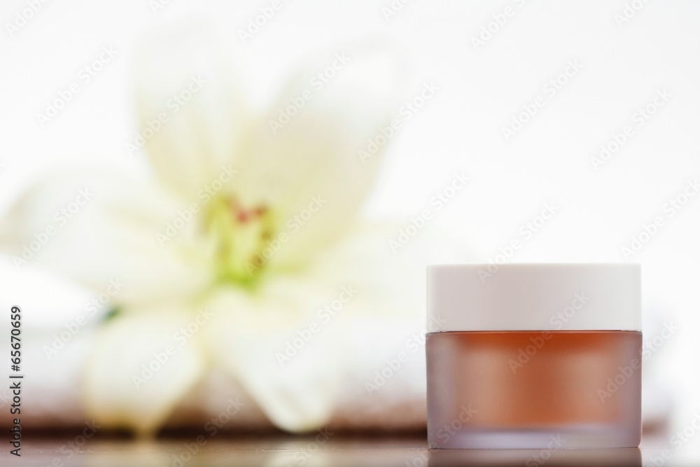 Skincare cream with white flower in background.