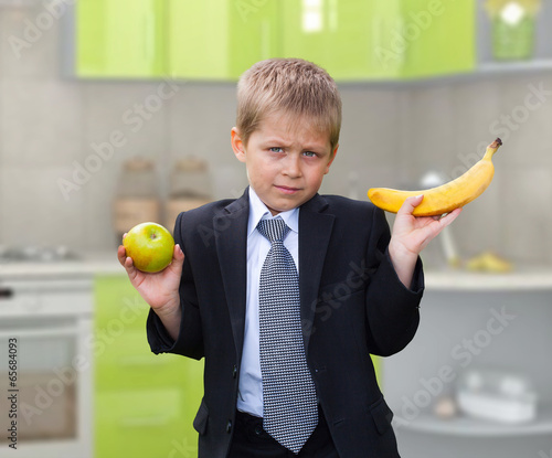 Fotografija schoolboy holding apple and banana, making choices, on kitchen b