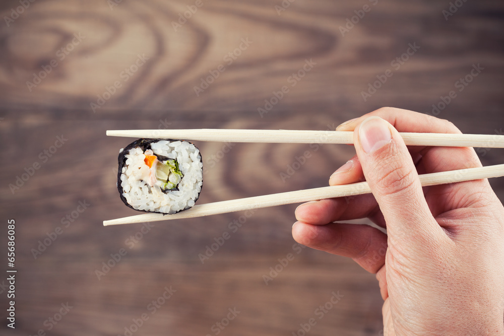 Hand holding sushi roll using chopsticks Hand holding sushi roll using chopsticks