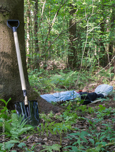 Shovel at the tree and man lying in the forest