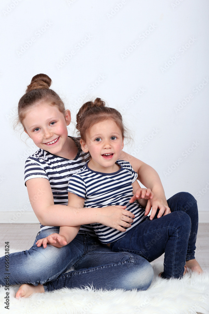 Beautiful small girls sitting on floor on wall background Beautiful small girls sitting on floor on wall background