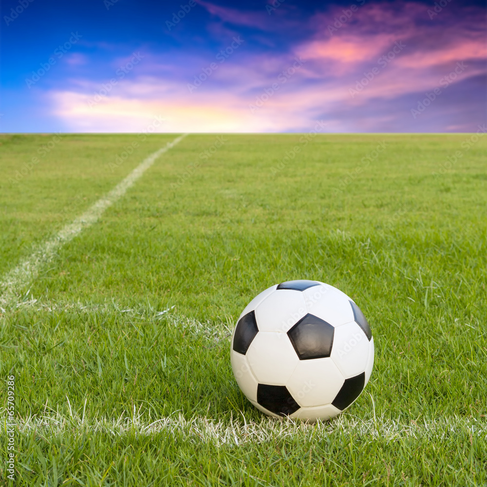 Naklejka premium soccer ball on soccer field against sunset sky
