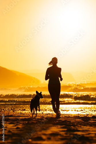 Woman and dog running on beach at sunrise © Dirima