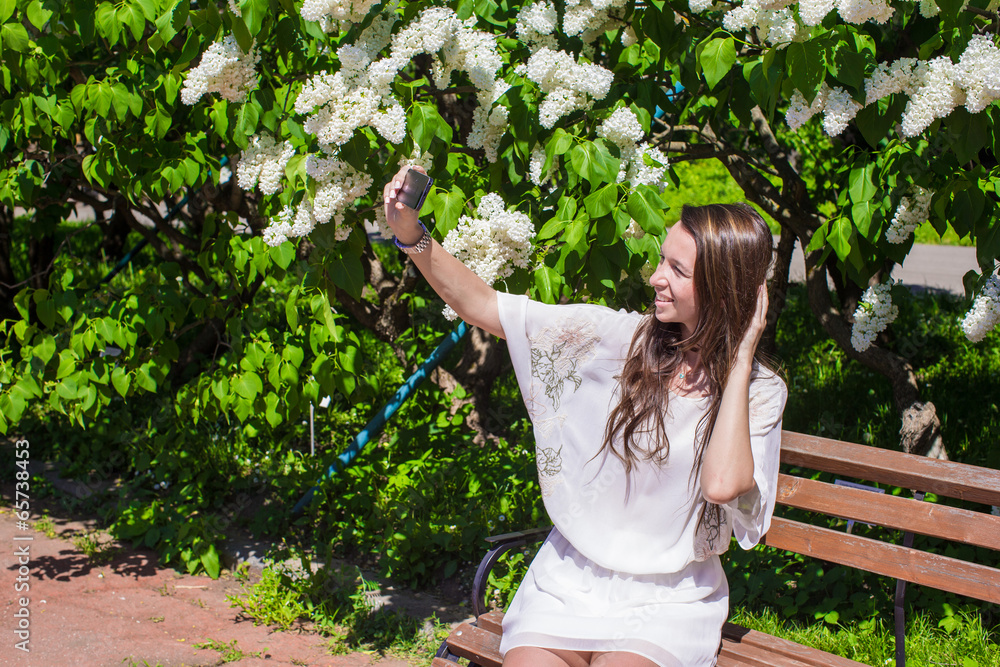 Naklejka premium Young woman take photo on her phone at blossoming lilac garden