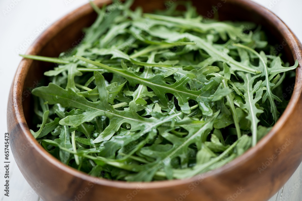 Fresh arugula lettuce in a wooden bowl, close-up, studio shot Fresh arugula lettuce in a wooden bowl, close-up, studio shot