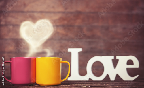 Two cups, abstract heart and word Love on wooden table.