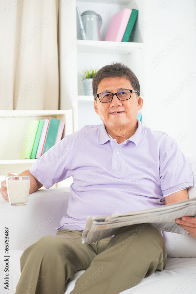 senior asian chinese reading newspaper and drinking milk on a so senior asian chinese reading newspaper and drinking milk on a so