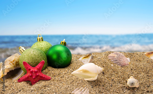 Christmas balls and shells on sand with summer sea background