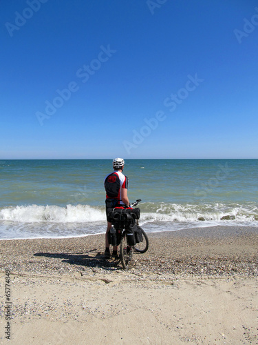 Man standing on the beach with bicycle.
