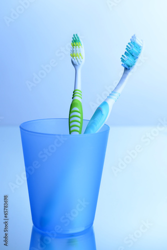 Toothbrushes in glass on light grey background