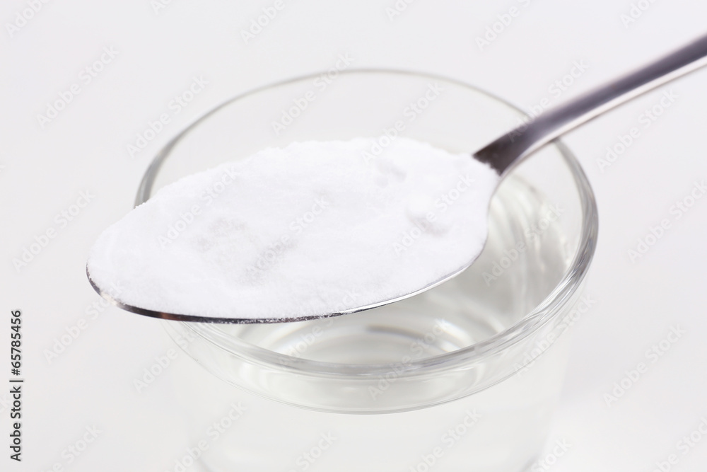 Spoon of baking soda over glass of water, isolated on white Spoon of baking soda over glass of water, isolated on white