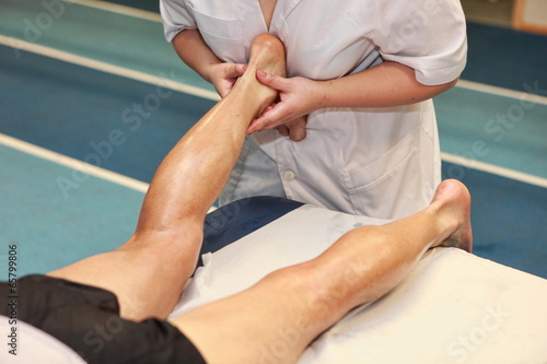 masseuse massaging athlete' s Achilles tendon after running photo