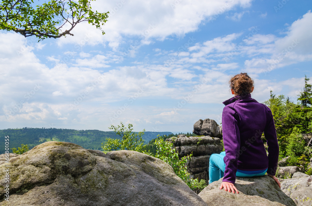 Lady sitting on a rock and admires the view in the mountains