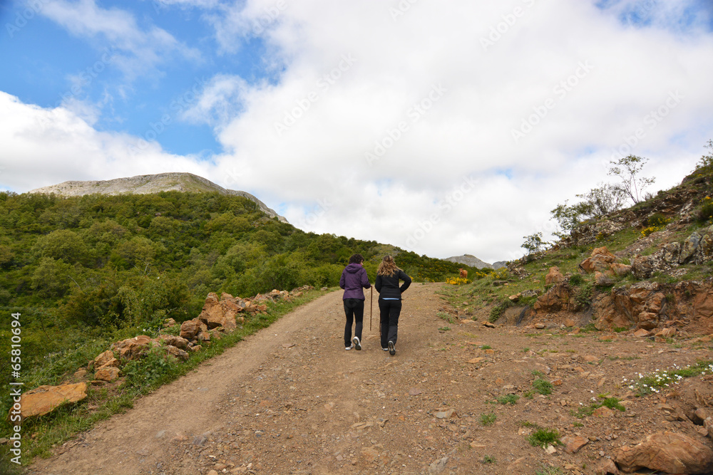 pareja de mujeres caminando por un camino de montaña