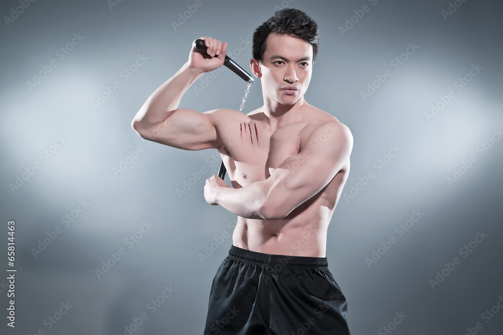 Muscled asian kung fu man in action pose with nunchucks. Blood s Stock