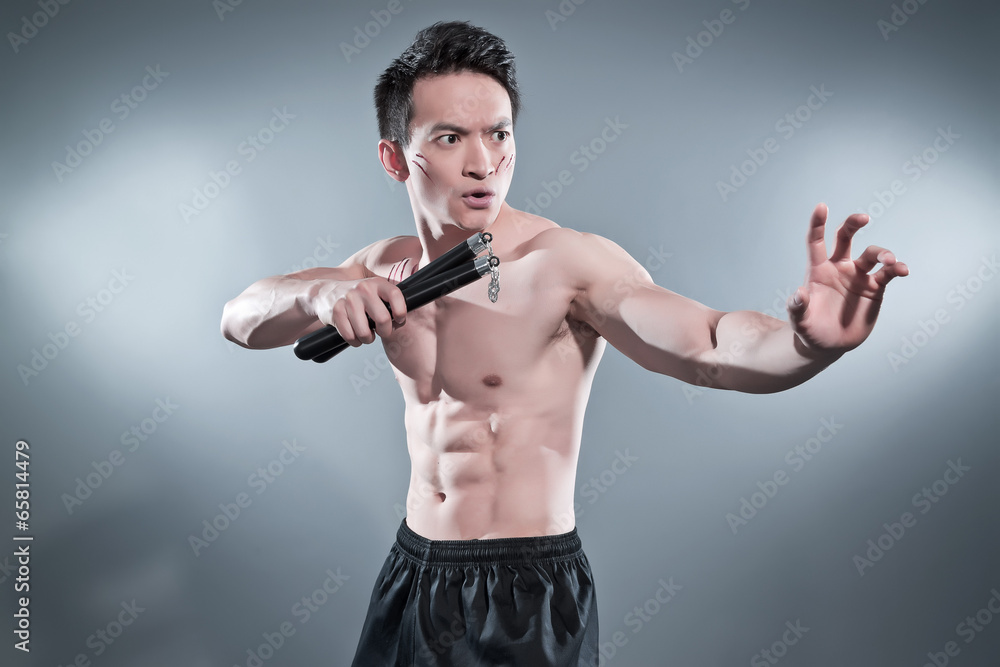 Muscled asian kung fu man in action pose with nunchucks. Blood s