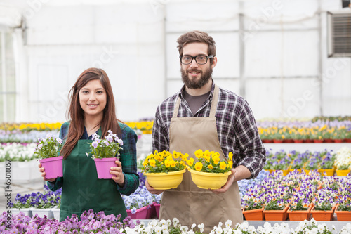 Portrait of young worker with potted flower at greenhouse