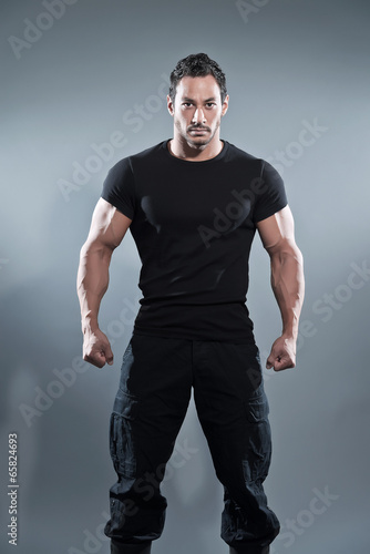 Combat muscled fitness man wearing black shirt and pants. Studio © ysbrandcosijn
