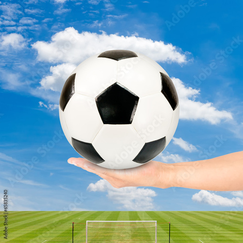 Soccer ball in hand with soccer field and blue sky