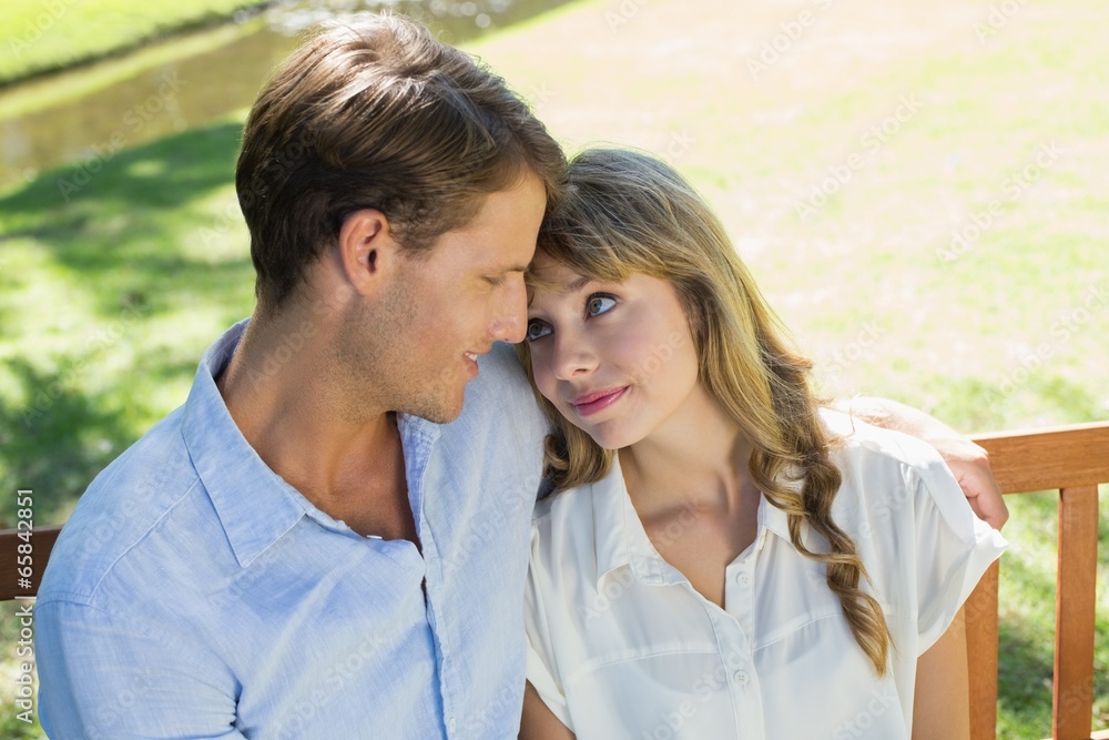 Cute couple sitting on park bench together looking at each other Cute couple sitting on park bench together looking at each other
