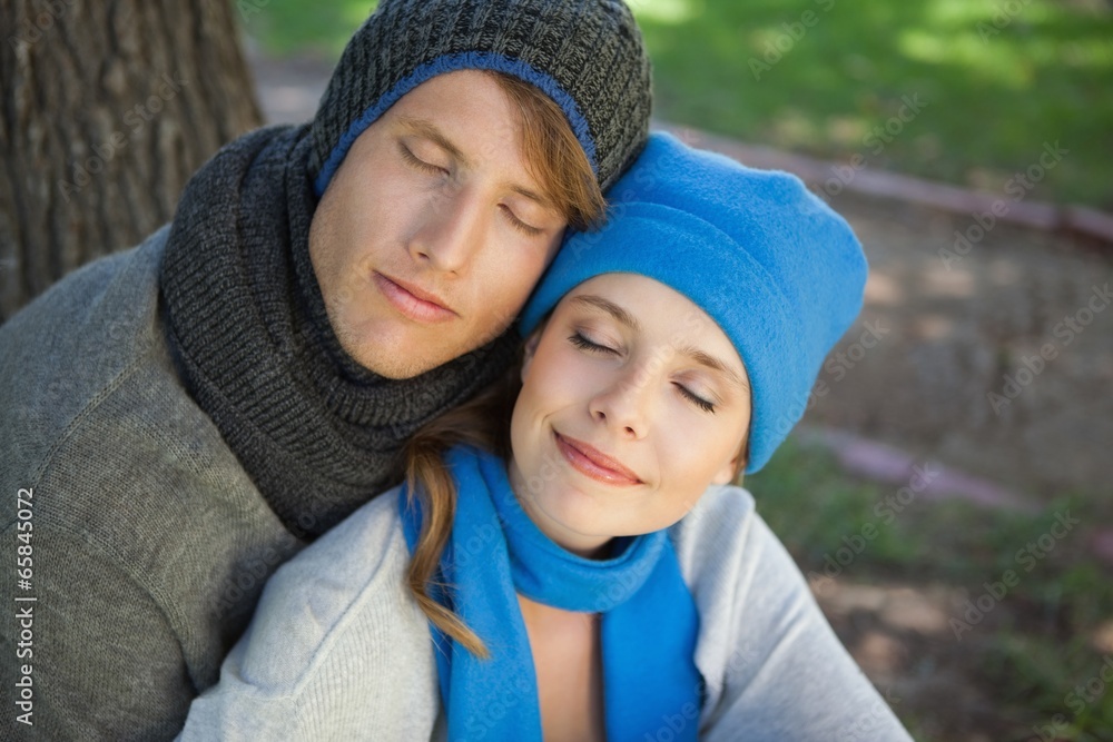 Cute couple sitting and embracing in the park with eyes closed Cute couple sitting and embracing in the park with eyes closed