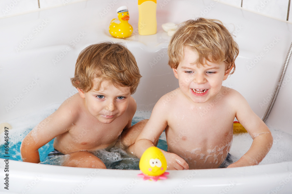 Two little twins boys having fun with water by taking bath in ba Two little twins boys having fun with water by taking bath in ba