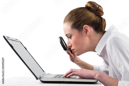 Businesswoman typing and looking through magnifying glass