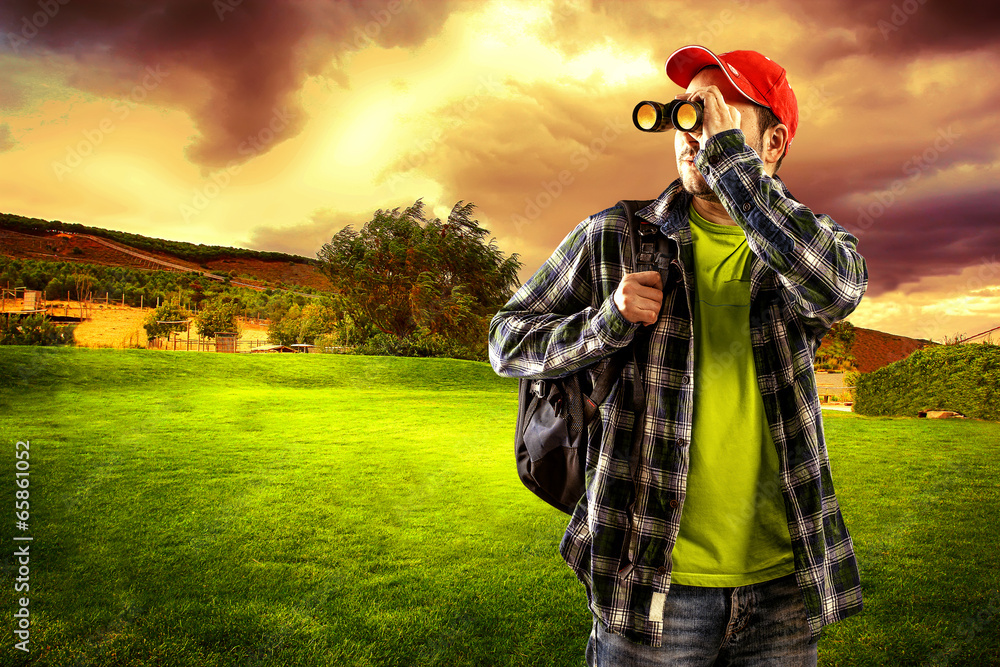 Man traveler looking in binocular standing on green valley