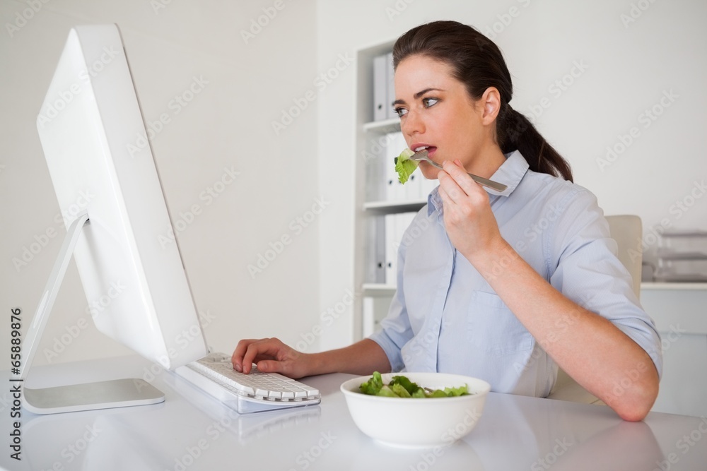 Casual brunette businesswoman eating a salad at her desk