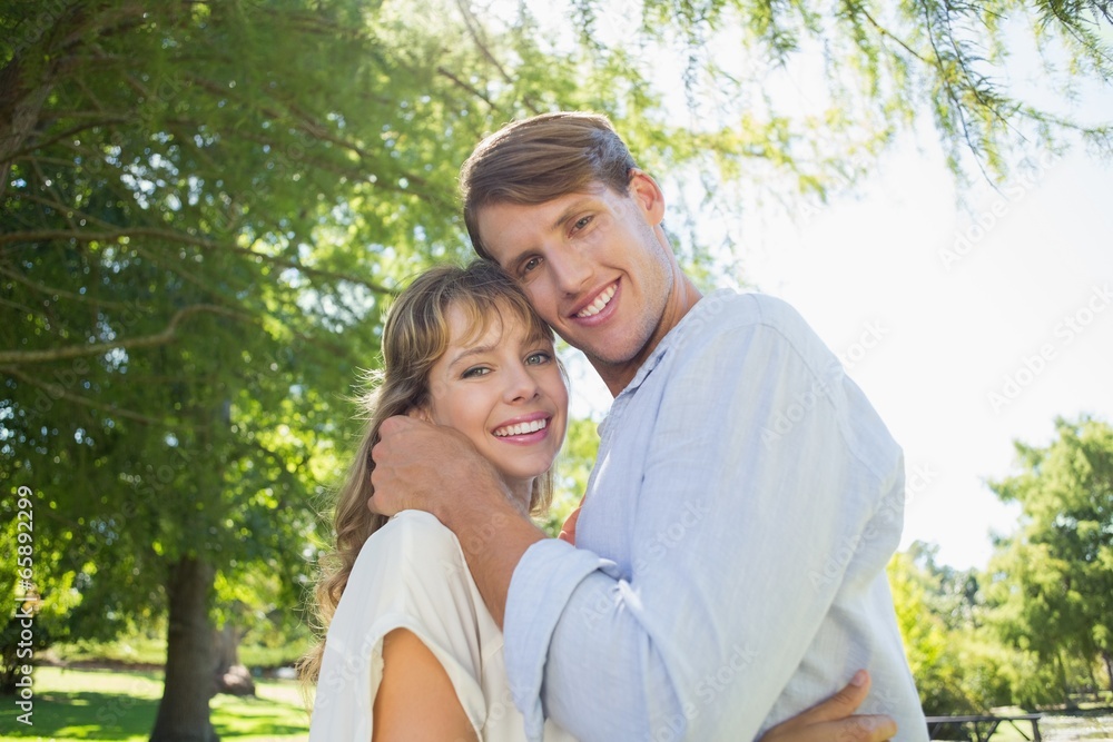 Cute couple hugging and smiling at camera in the park Cute couple hugging and smiling at camera in the park