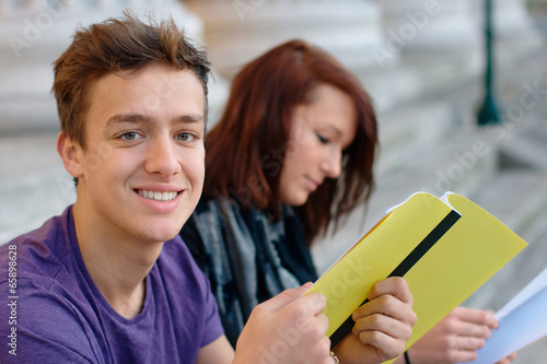 Smiling teenage student outdoors with a girl at the background