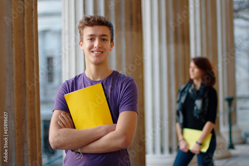 Smiling teenage student outdoors with a girl at the background