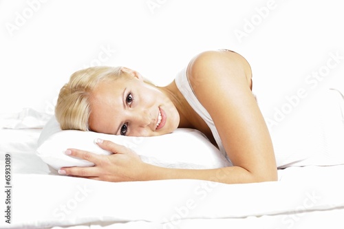 Light hair female model, smiling and lying on the pillow.