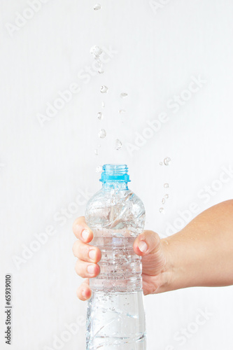 Female hand shaking a small bottle of fresh water with a splash