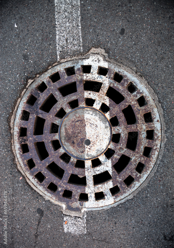 Manhole with metal cover in asphalt with white road marking line