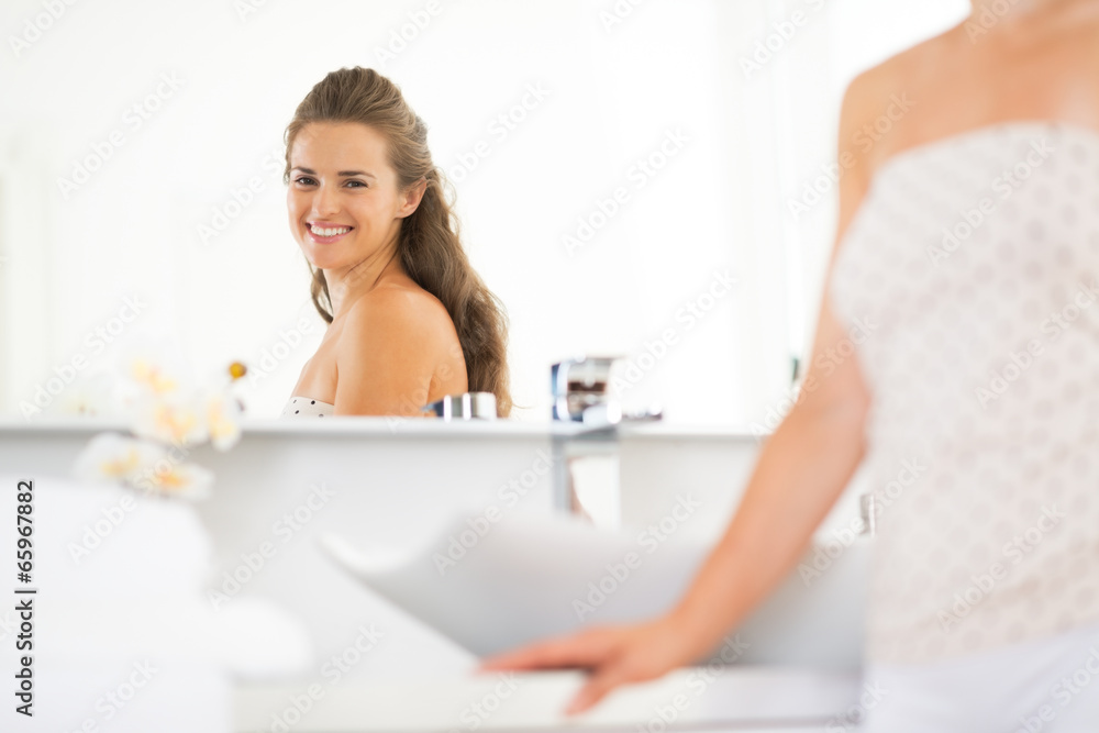 Happy young woman looking in mirror in bathroom Happy young woman looking in mirror in bathroom