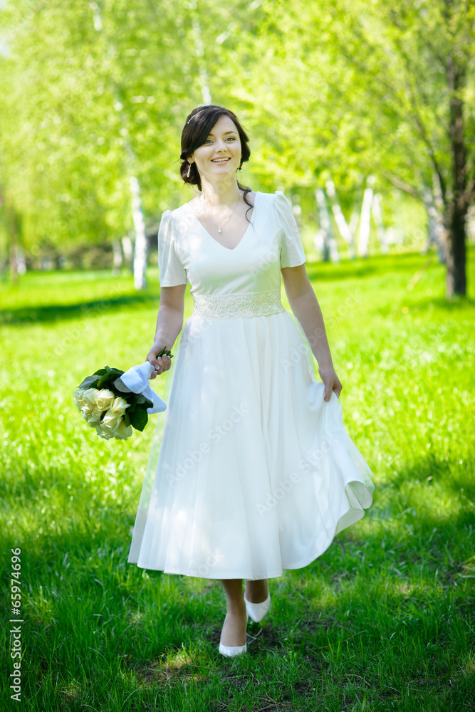 Beautiful bride walking on green grass holding bouquet of roses Beautiful bride walking on green grass holding bouquet of roses