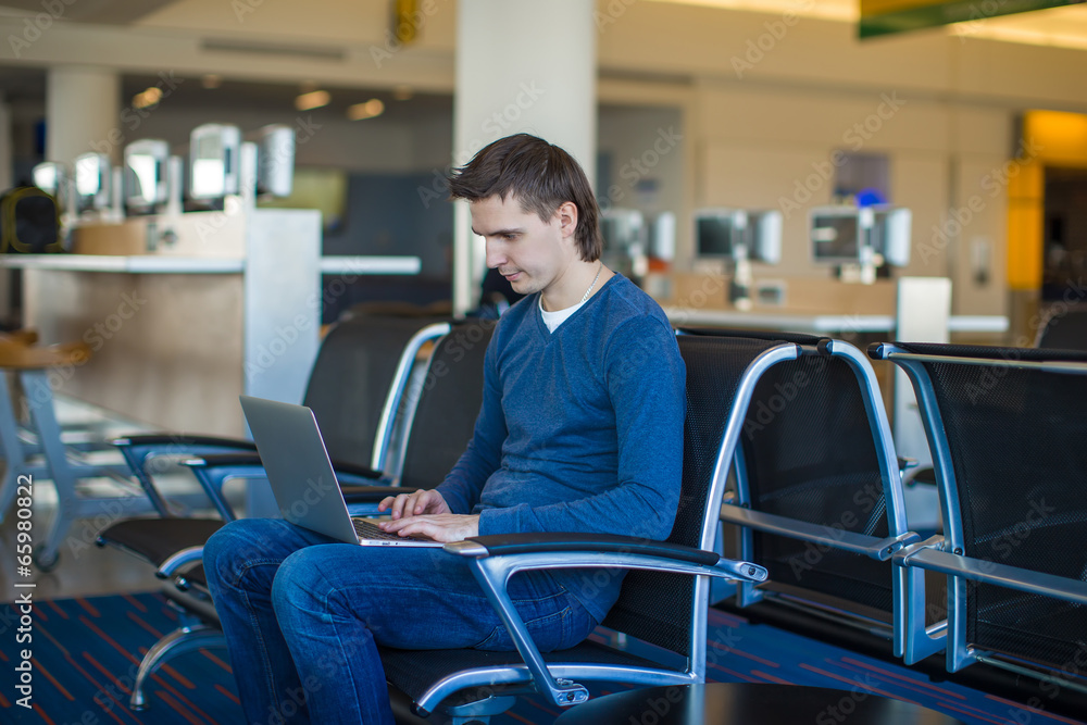 Young man with a laptop at the airport while waiting his flight Young man with a laptop at the airport while waiting his flight