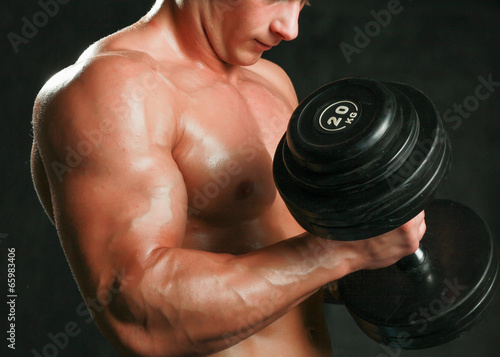 Handsome muscular man working out with dumbbells over black